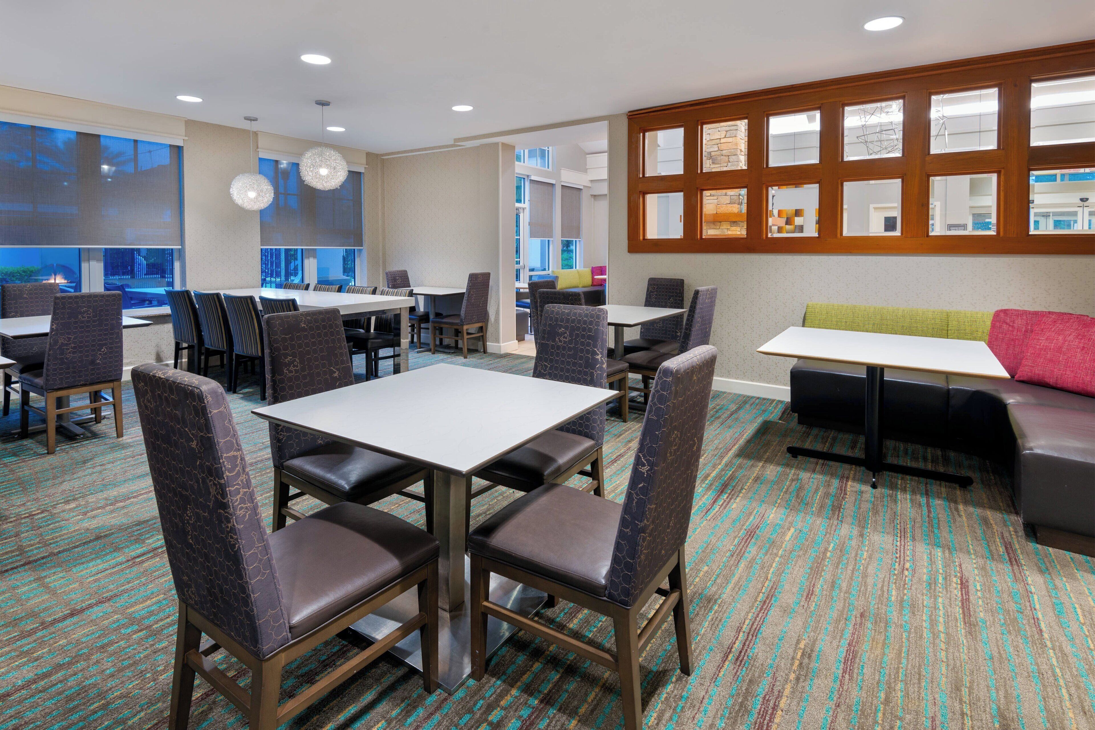 Un hall d’hôtel doté de plusieurs espaces aménagés avec des sièges, notamment des tables et des chaises, un canapé et une grande fenêtre offrant une vue panoramique.