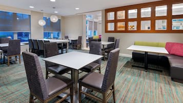 Um saguão de hotel com várias áreas de estar, incluindo mesas e cadeiras, um sofá e uma janela grande com vista.