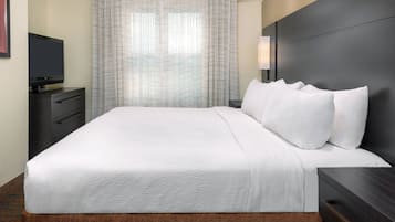 A hotel room with a large bed, a flat-screen TV on a dresser, and a window with sheer curtains.