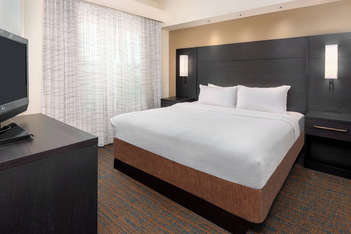 A hotel room with a large bed, a desk with a telephone, and a headboard with wall-mounted lights.