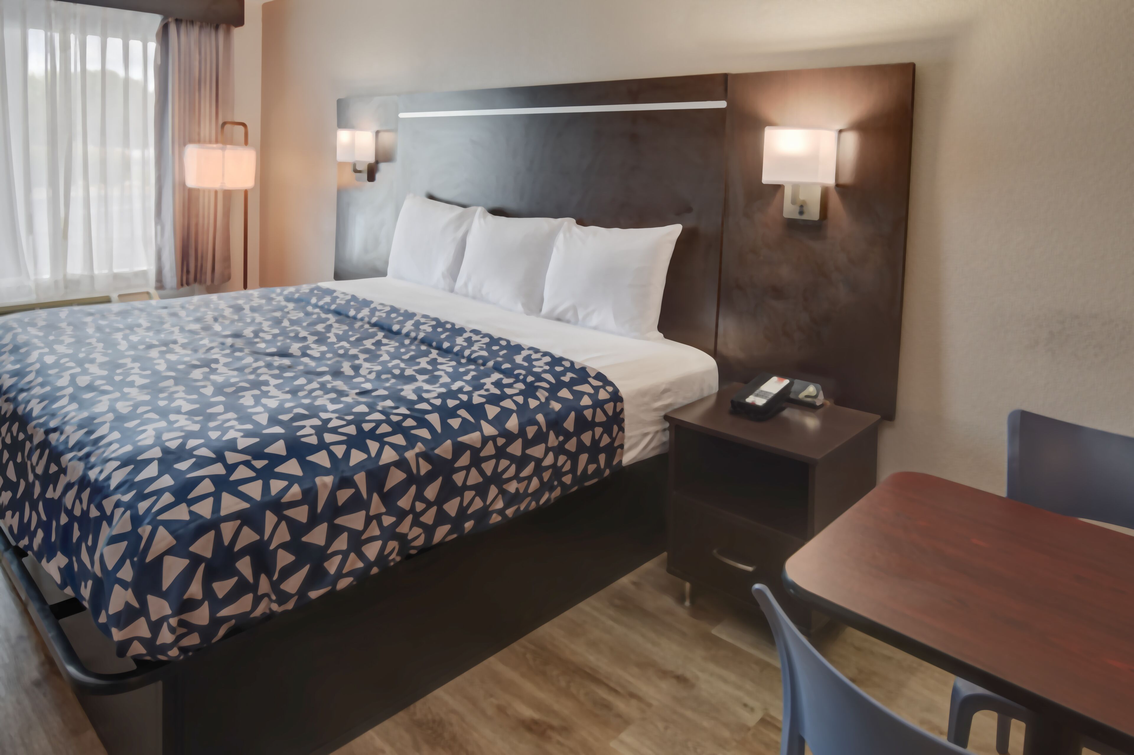 A hotel room with a bed, bedside table, lamp, and a small table with chairs.