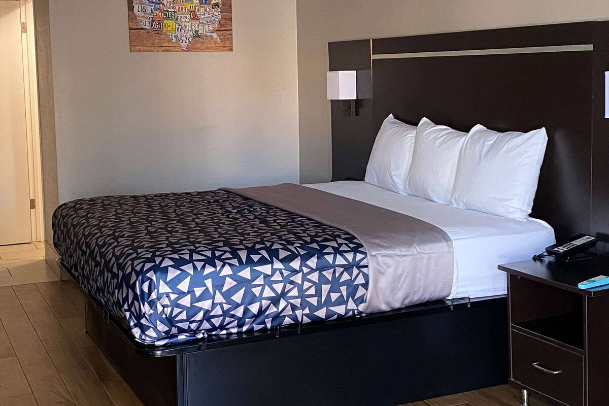 A hotel room with a bed, a nightstand, and a wall-mounted lamp.