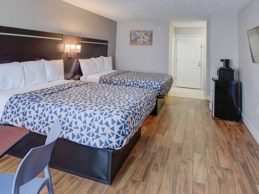 Ein Hotelzimmer mit zwei Betten, einem Schreibtisch und einem Sessel. Eine Tür führt in einen weiteren Raum, und ein kleiner Tisch mit einer Kaffeemaschine steht bereit.