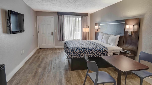 Una habitación de hotel con cama, escritorio, dos sillas, televisor y puerta.