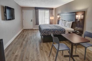 Una habitación de hotel con cama, escritorio, dos sillas, televisor y puerta.