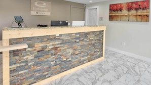 Una zona de recepción con mostrador de mosaico de piedra, una laptop, una tableta y un cuadro con árboles.