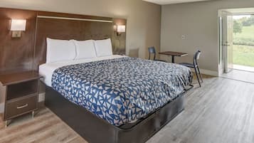 Habitación de hotel con una cama grande, una mesita de noche, un escritorio y una silla. Hay una puerta que da a un balcón con vistas al exterior.