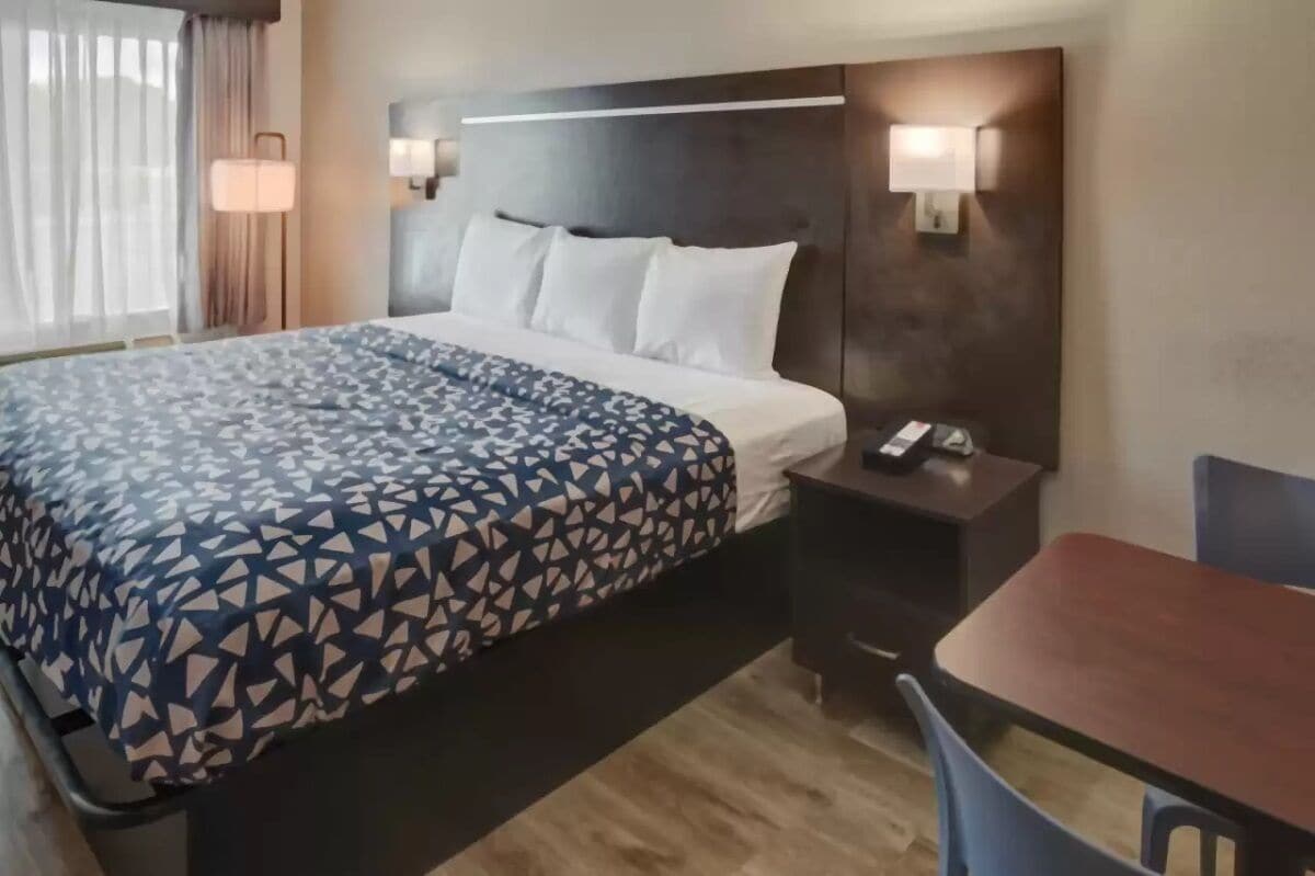 Ein Hotelzimmer mit Bett, Nachttisch, Lampe und einem kleinen Tisch mit Stühlen.