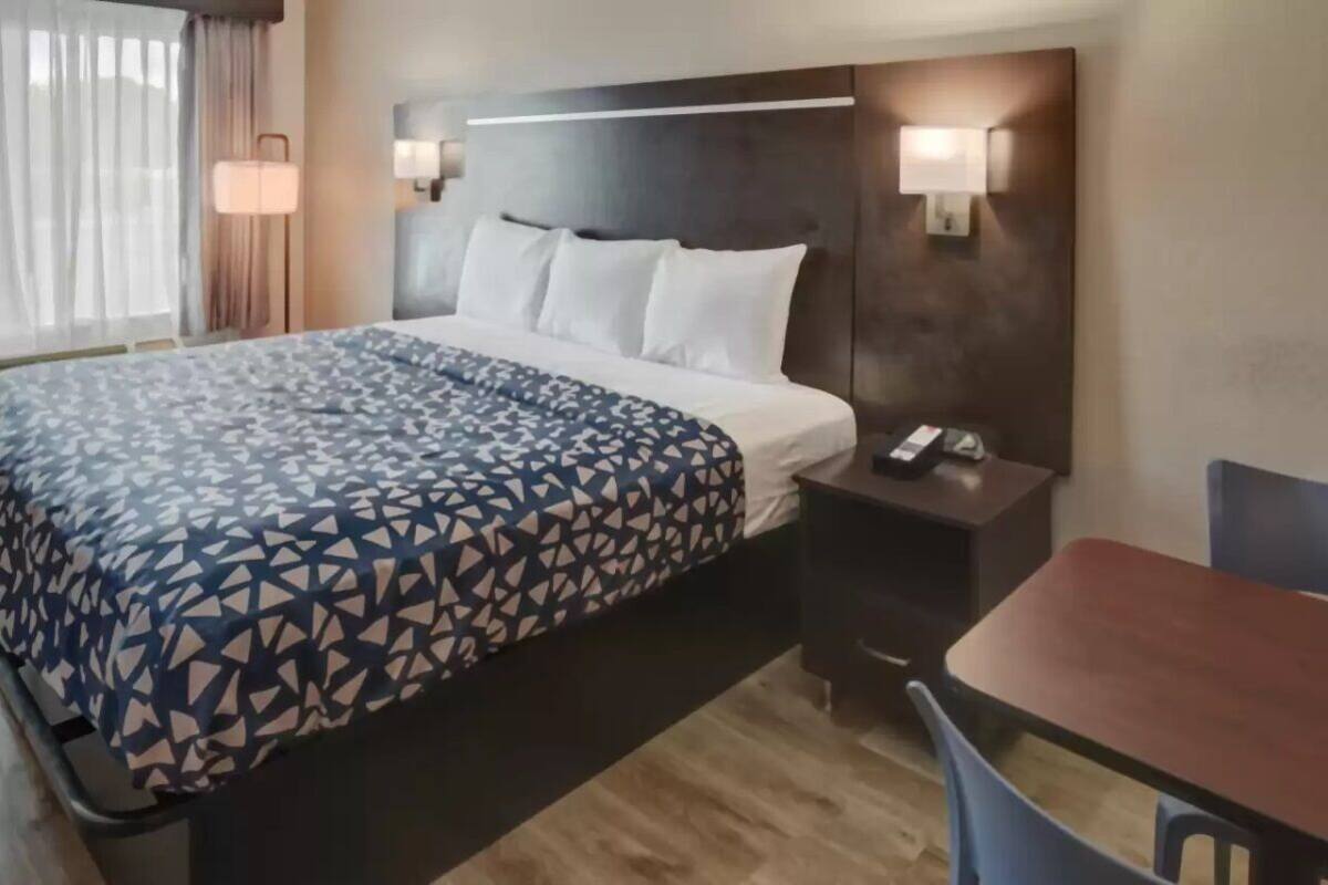 A hotel room with a bed, bedside table, lamp, and a small table with chairs.