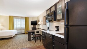 Habitación de hotel con cama, escritorio, silla, refrigerador, microondas, cafetera y televisión.