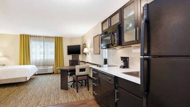 A hotel room with a bed, a desk, a chair, a refrigerator, a microwave, a coffee maker, and a television. - Candlewood Suites Washington North by IHG (Washington)