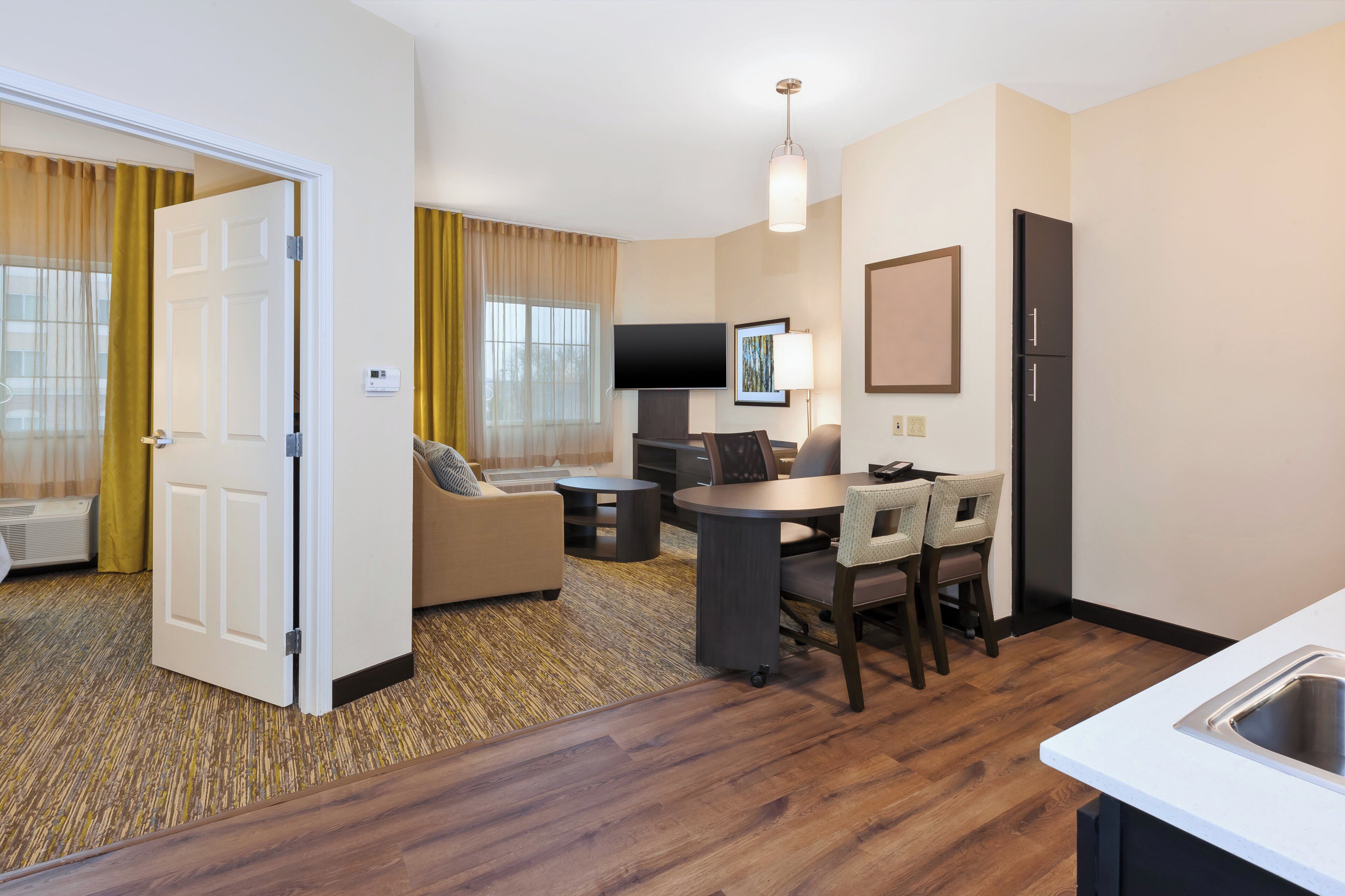 Ein Hotelzimmer mit Essbereich, einer Couch, einem Fernseher und einer Küchenzeile.