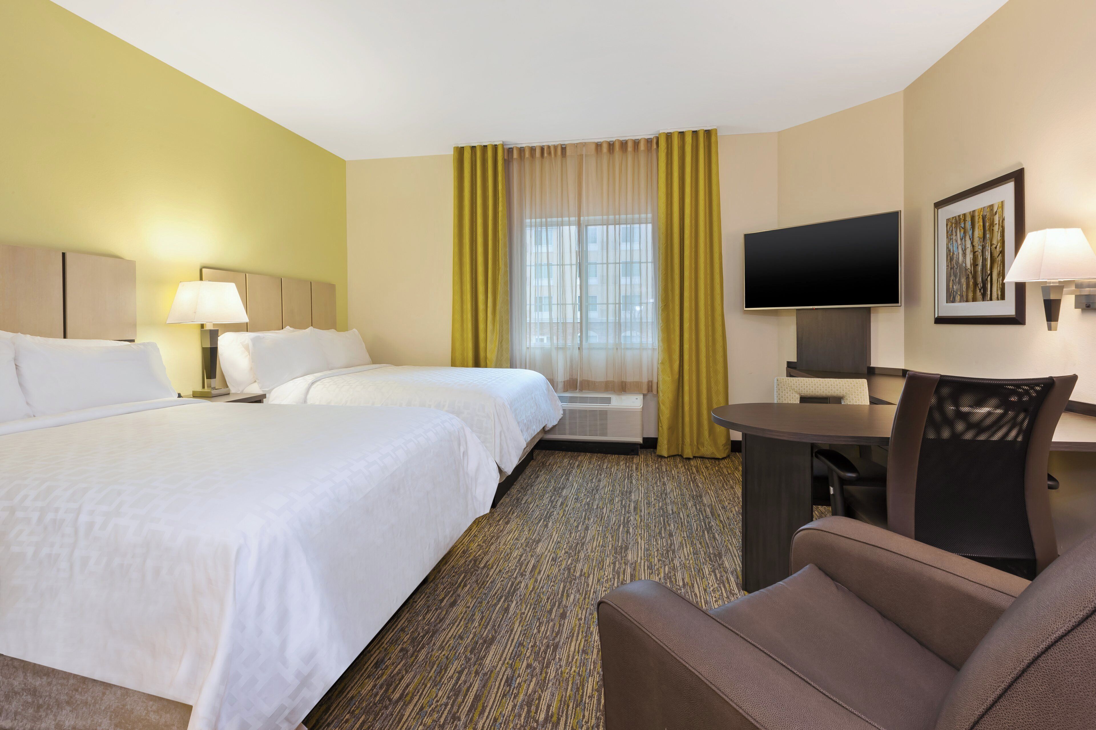 A hotel room with two beds, a desk, a chair, a television, and a window with curtains.