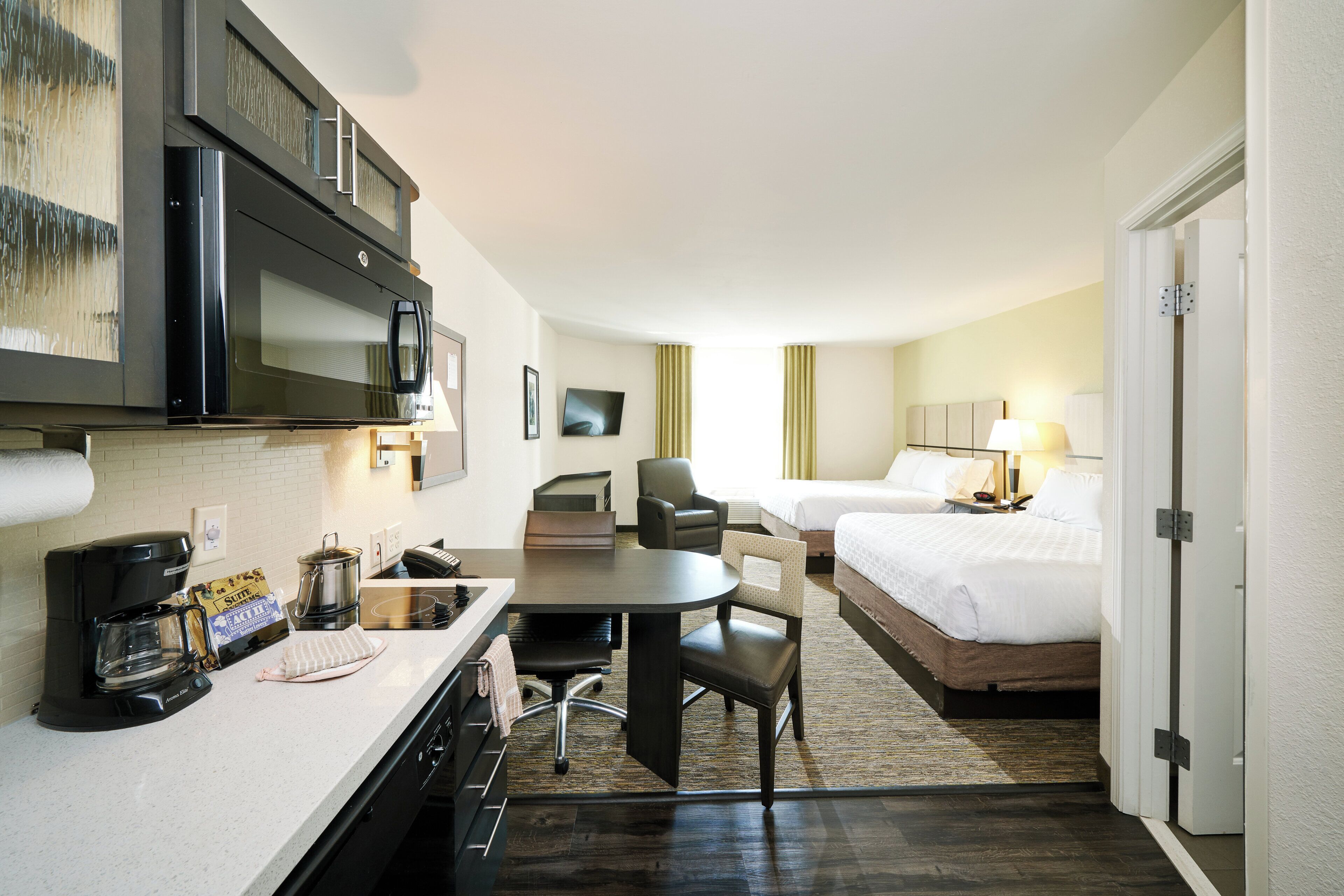 A hotel room with a kitchenette, a dining area, a bed, and a bathroom.