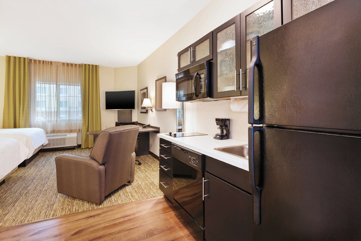 A hotel room with a bed, a sofa, a desk, a refrigerator, a microwave, a television, and a window with curtains.