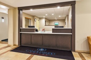 A reception area with a dark wood reception desk, a black doormat with "CANDLEWOOD SUITES" logo, and a clock on the wall. - Candlewood Suites Washington North by IHG (Washington)