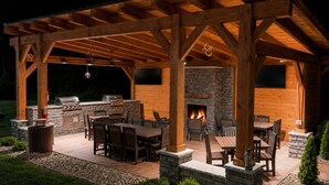 An outdoor patio with a stone fireplace, wooden tables and chairs, and a grill area. - Candlewood Suites Washington North by IHG (Washington)
