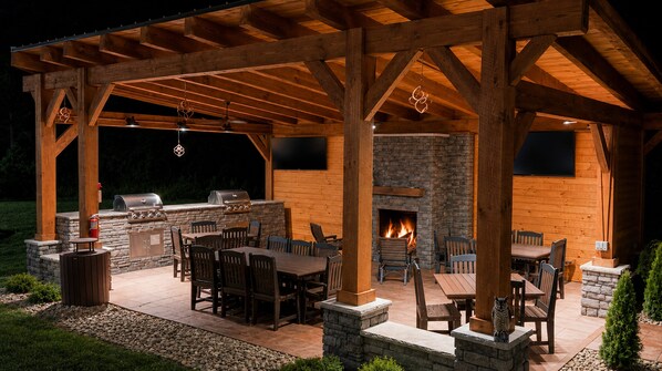 An outdoor patio with a stone fireplace, wooden tables and chairs, and a grill area. - Candlewood Suites Washington North by IHG (Washington)