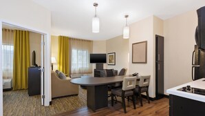A modern hotel room with a dining area, a flat-screen TV, a sofa, and a kitchen area with a stove. - Candlewood Suites Washington North by IHG (Washington)