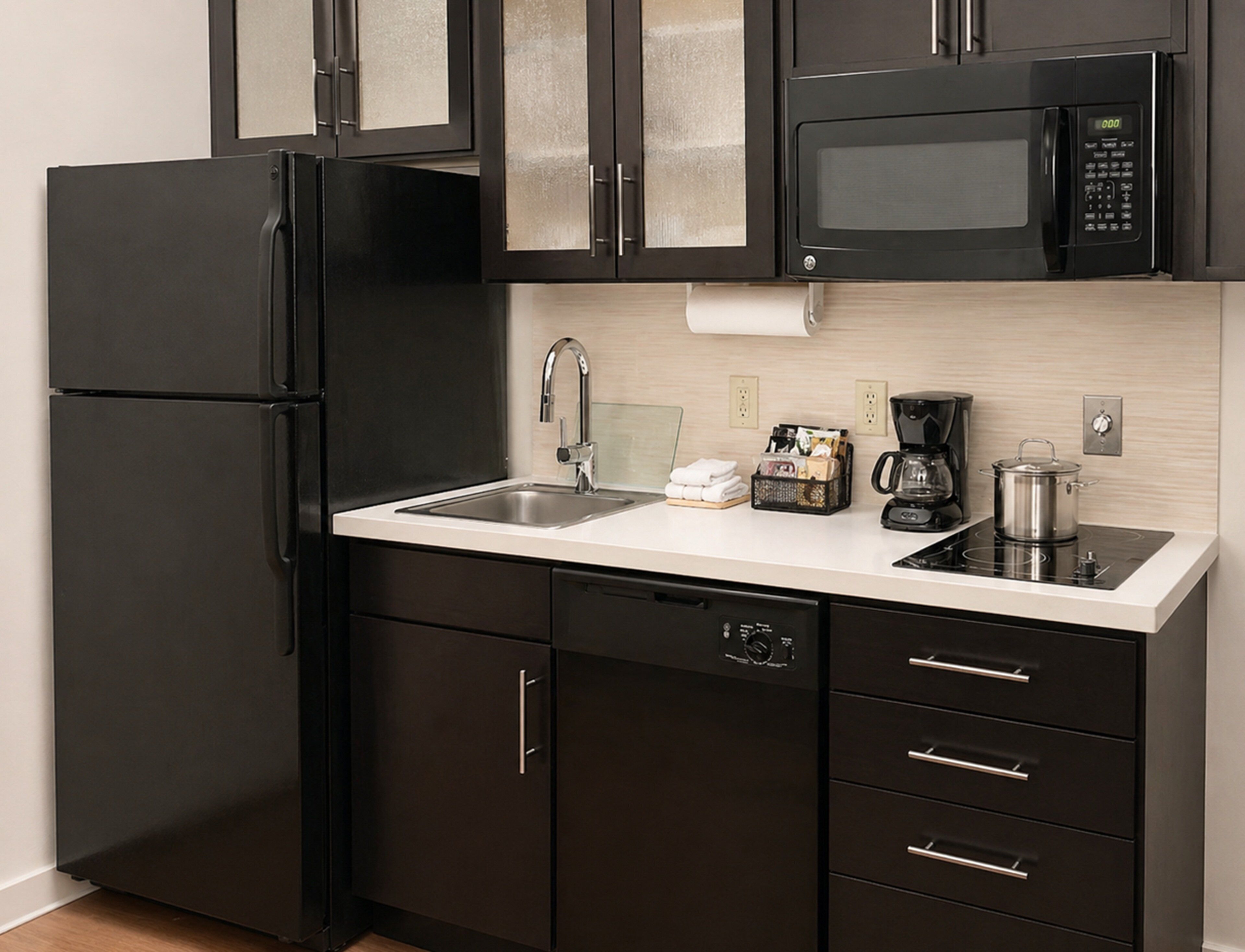 A modern kitchen with black cabinetry, a stainless steel refrigerator, a microwave, a sink, and a coffee maker.