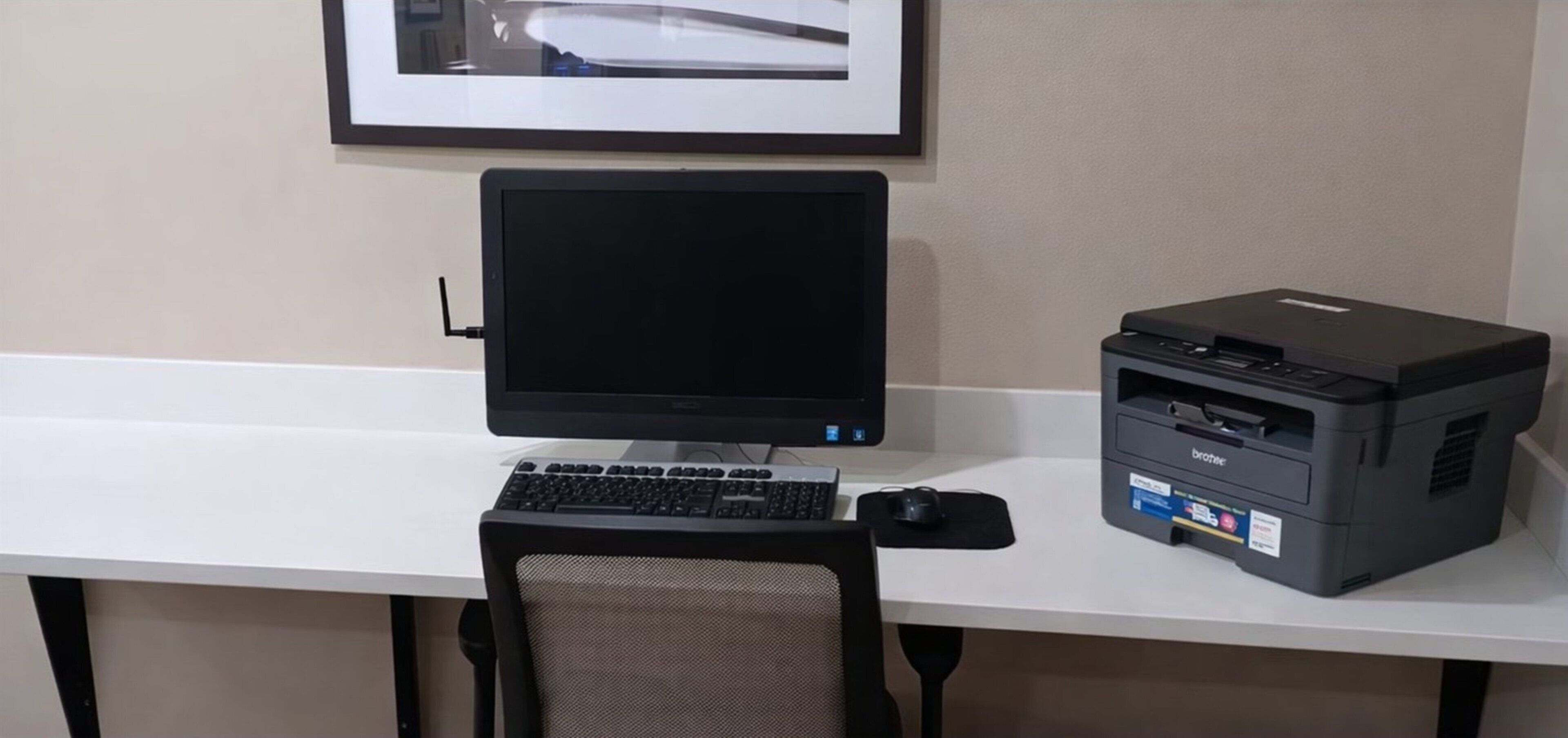 Uma mesa com monitor de computador, teclado, rato e impressora.