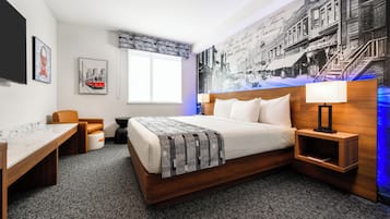 A hotel room with a bed, a desk, a chair, a nightstand, a lamp, and a large wall mural.