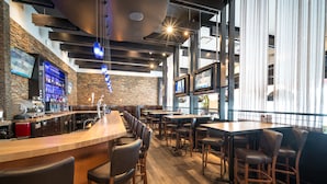 A modern bar area with a long counter, multiple seating options, and a brick wall with a digital screen.