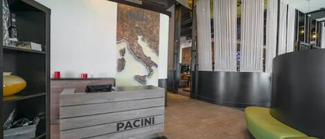 A reception area with a wooden desk labeled "PACINI," a green sofa, and a wall with a map.