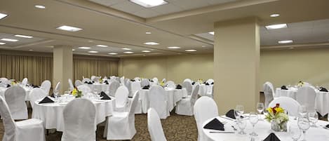 A banquet hall with round tables, white chairs, and a carpeted floor.