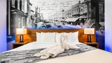 A hotel room with a bed, two bedside tables, a headboard, and a large wall mural of a street scene.