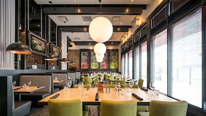 A restaurant with green upholstered chairs, a large wooden table, and multiple televisions on the walls.