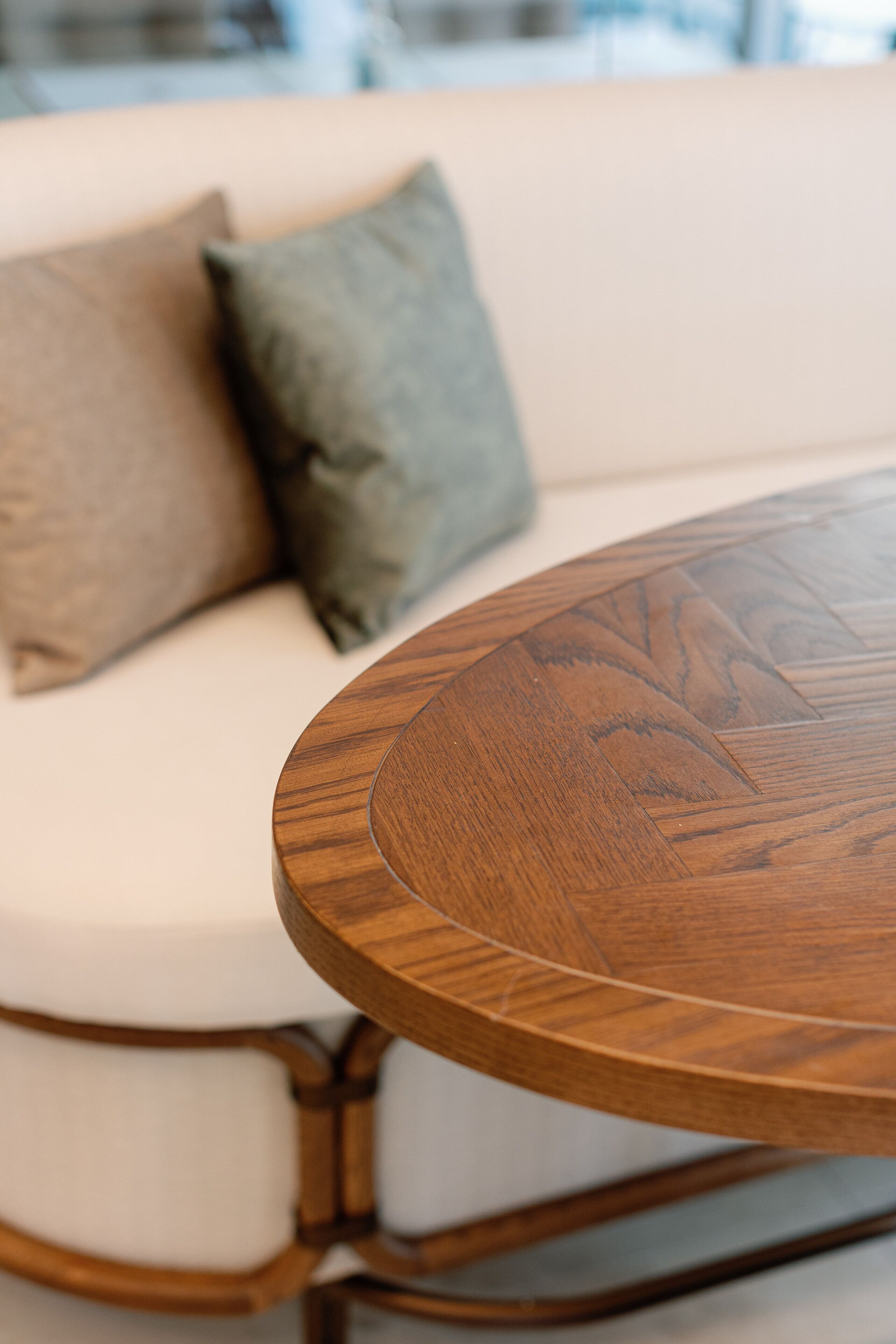 Een ronde houten tafel met een gebogen rand, geplaatst voor een witte bank met twee kussens.