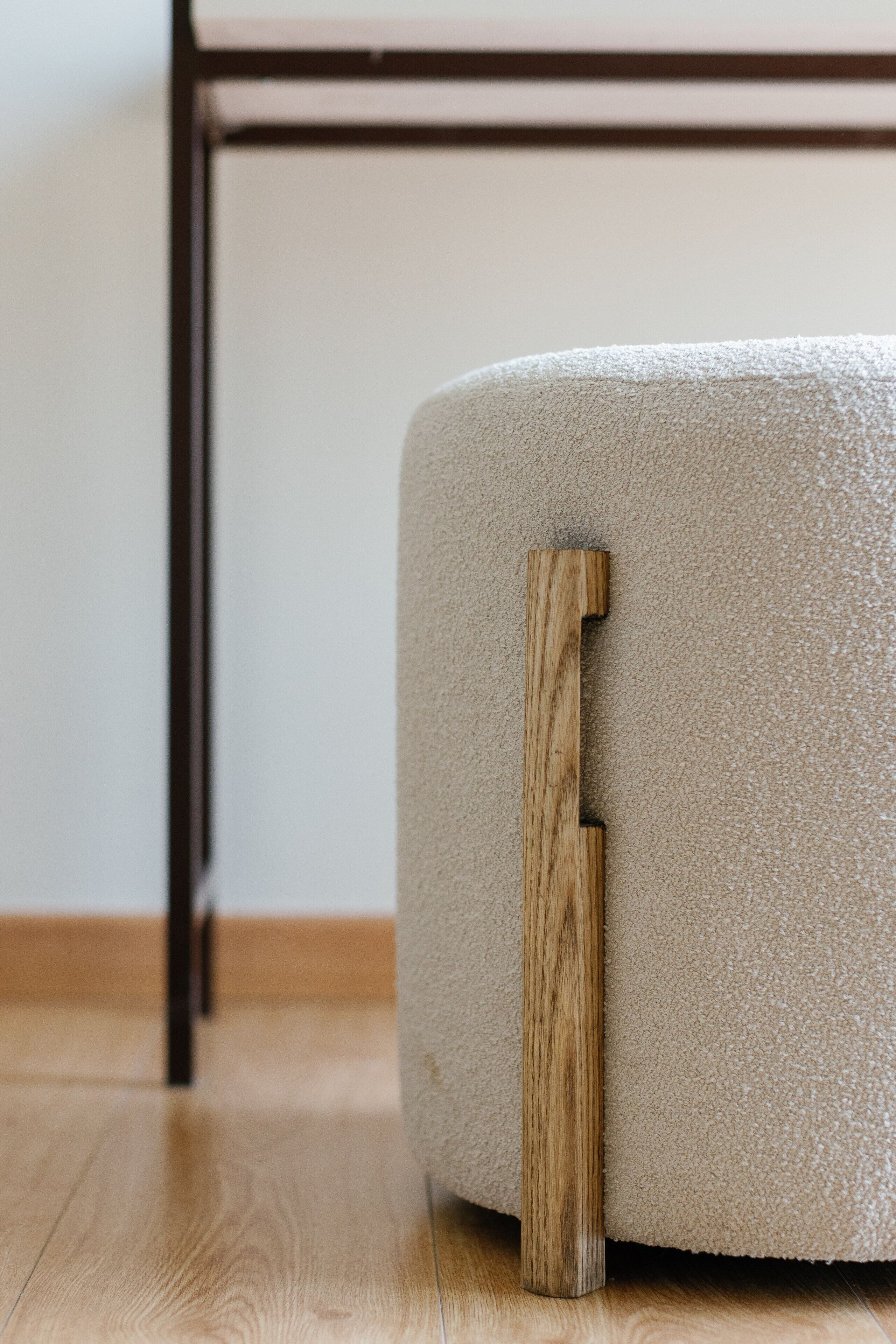 A corner of a room with a wooden floor, a beige textured ottoman, and a black metal table leg.