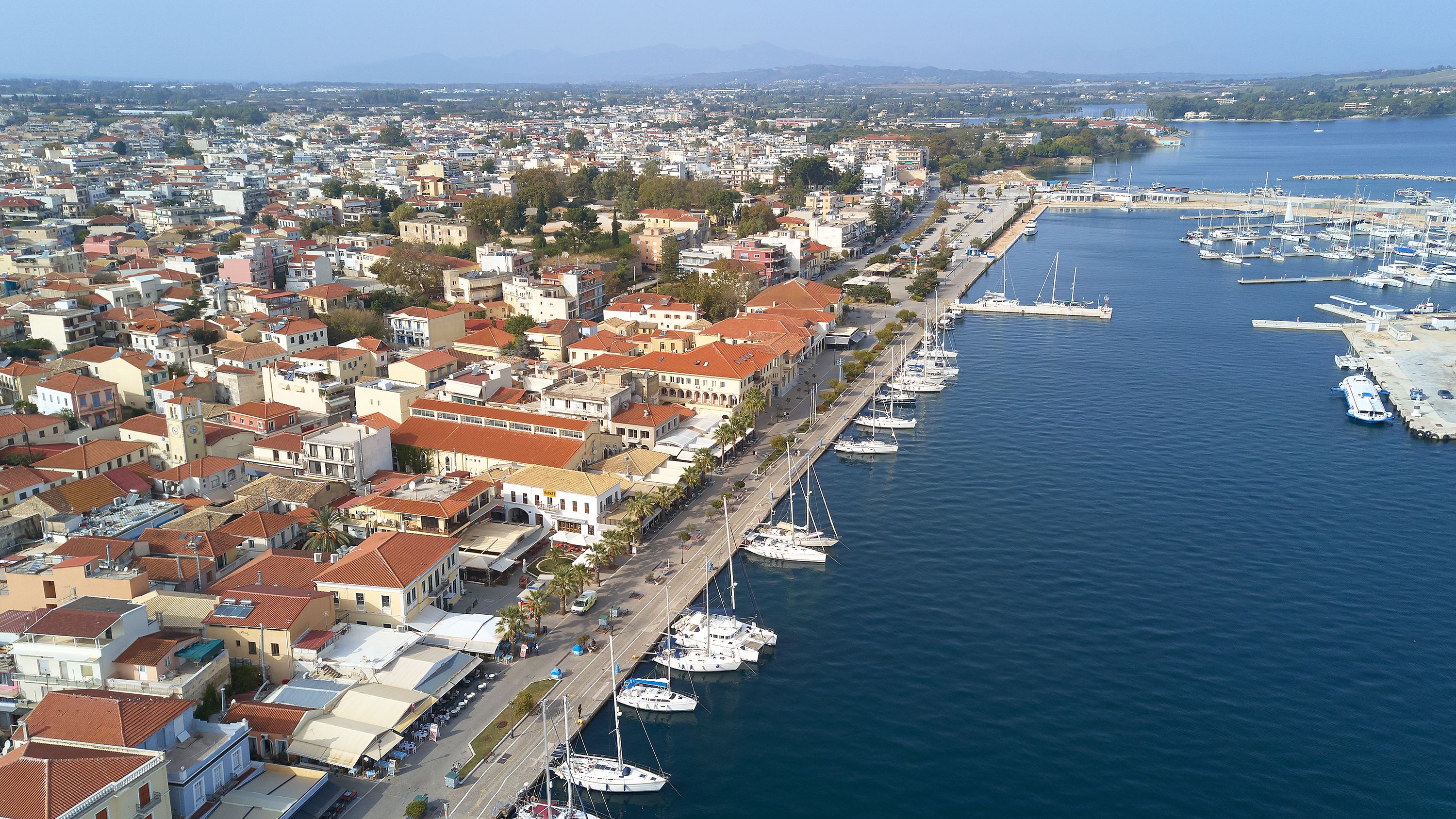 A coastal town with a marina filled with boats, buildings with red-tiled roofs, and a clear view of the sea.