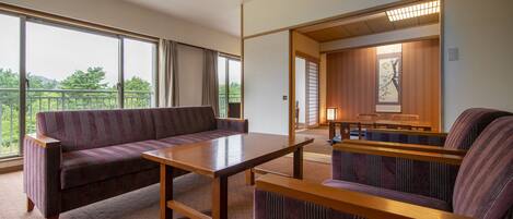 A modern hotel room with a large window, a sofa, a wooden table, and a view of the outdoors.