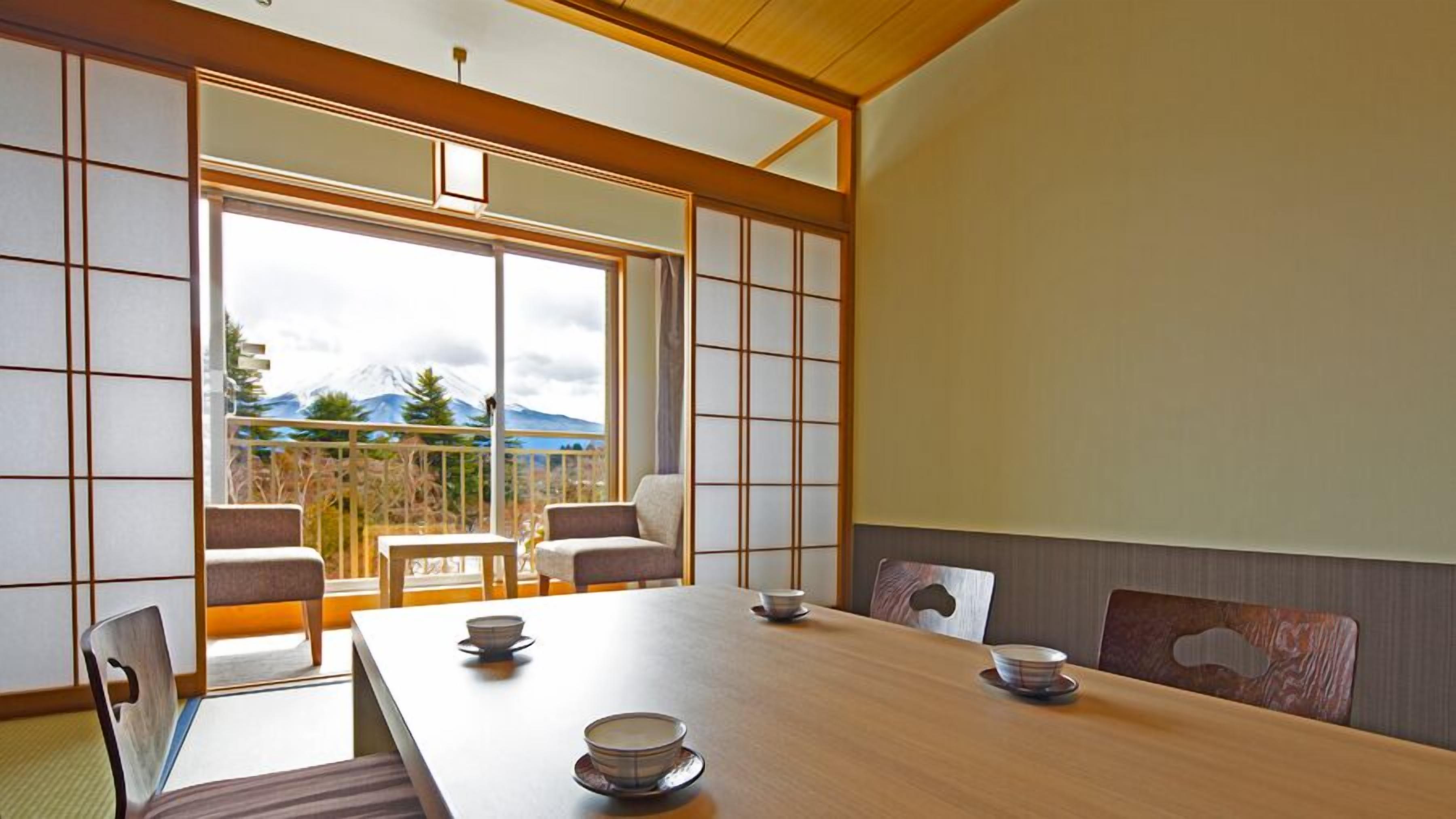 A traditional Japanese-style room with tatami flooring, a low table with bowls, and a sliding door leading to a balcony with a mountain view.