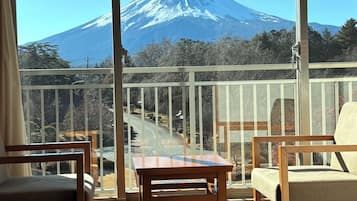 A room with a view of a snow-capped mountain, a balcony with a railing, and two chairs and a small table.