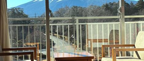 A room with a view of a snow-capped mountain, a balcony with a railing, and two chairs and a small table.