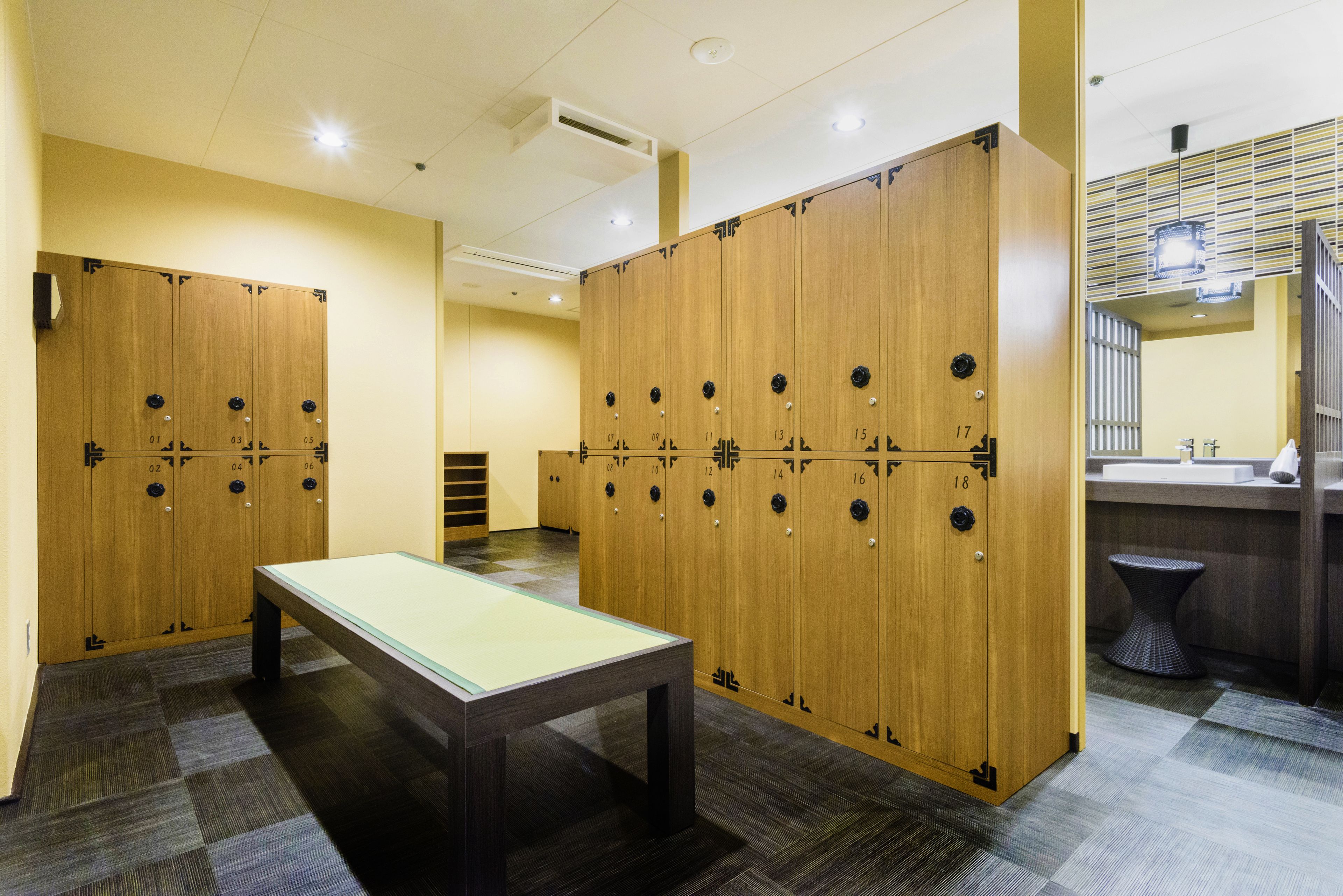 A locker room with multiple wooden lockers, a glass-top table, and a small stool.