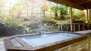 Un espace de sources chaudes doté d’une terrasse en bois, d’un bain à remous en pierre et entouré de verdure.