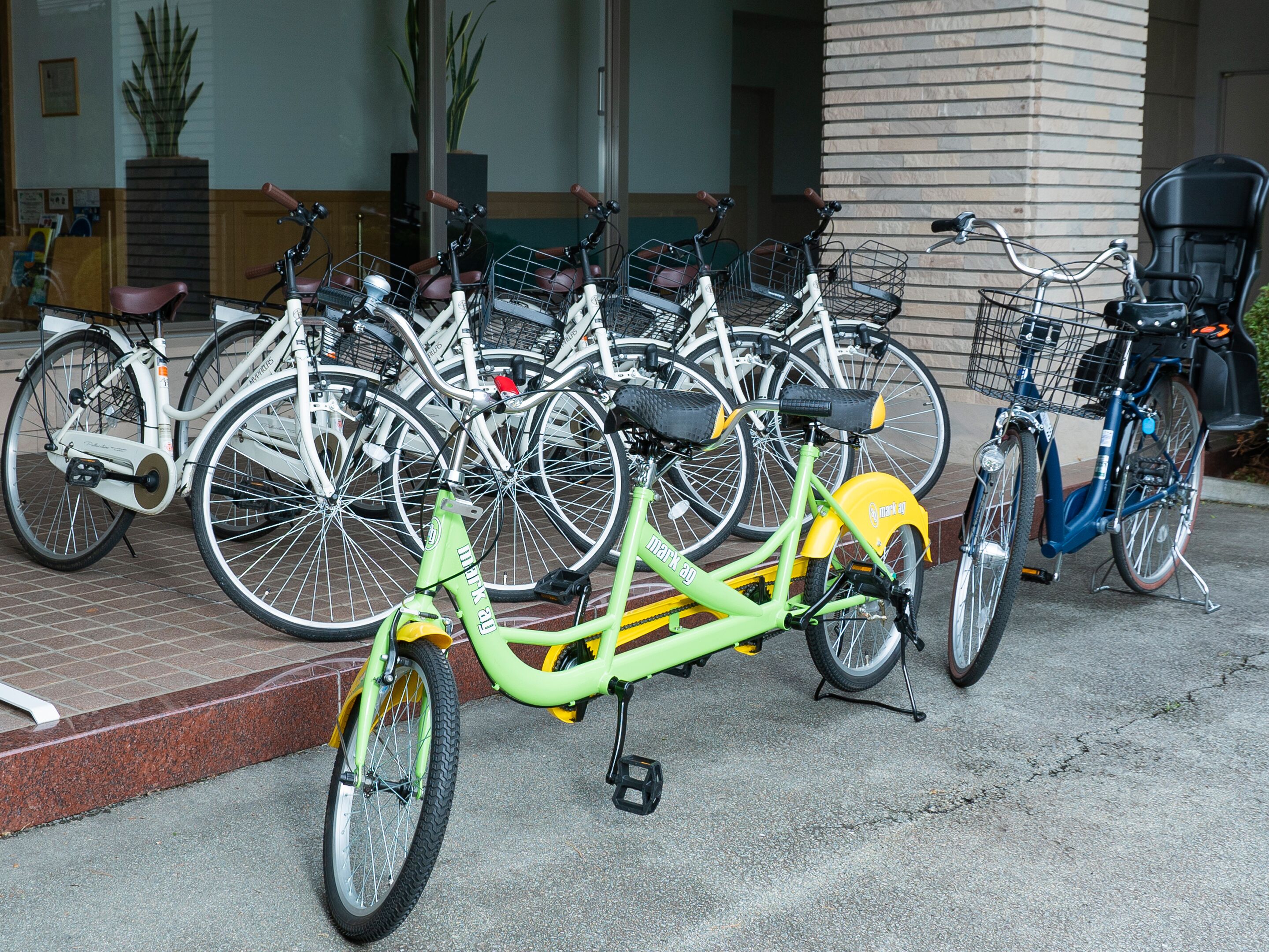 Een rij fietsen geparkeerd voor een gebouw met een bakstenen gevel en een grote kolom.