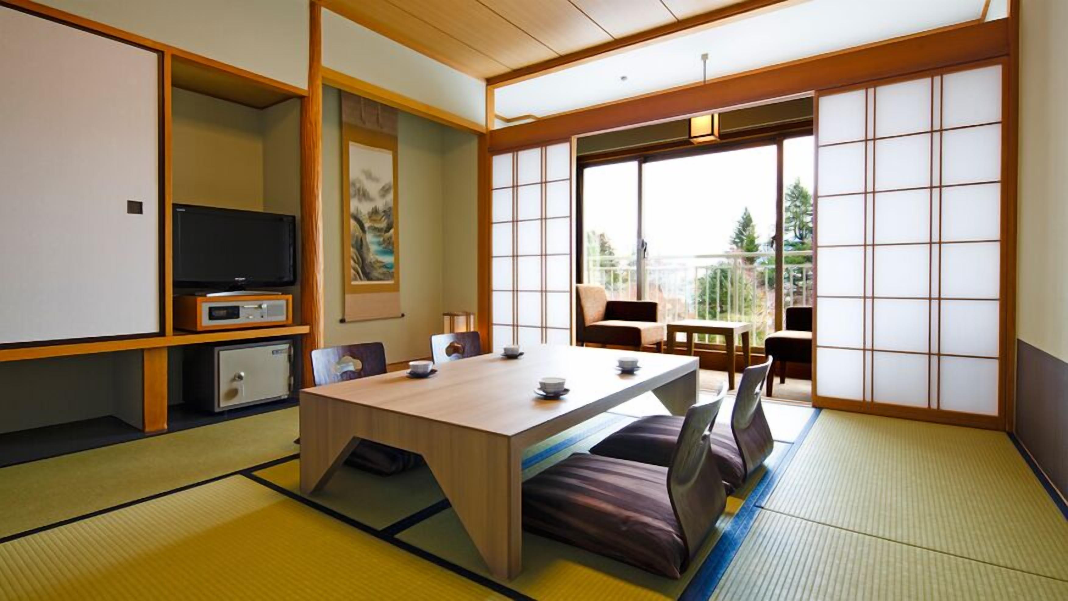 A traditional Japanese-style room with tatami flooring, a low table with cushions, a television, and sliding doors.