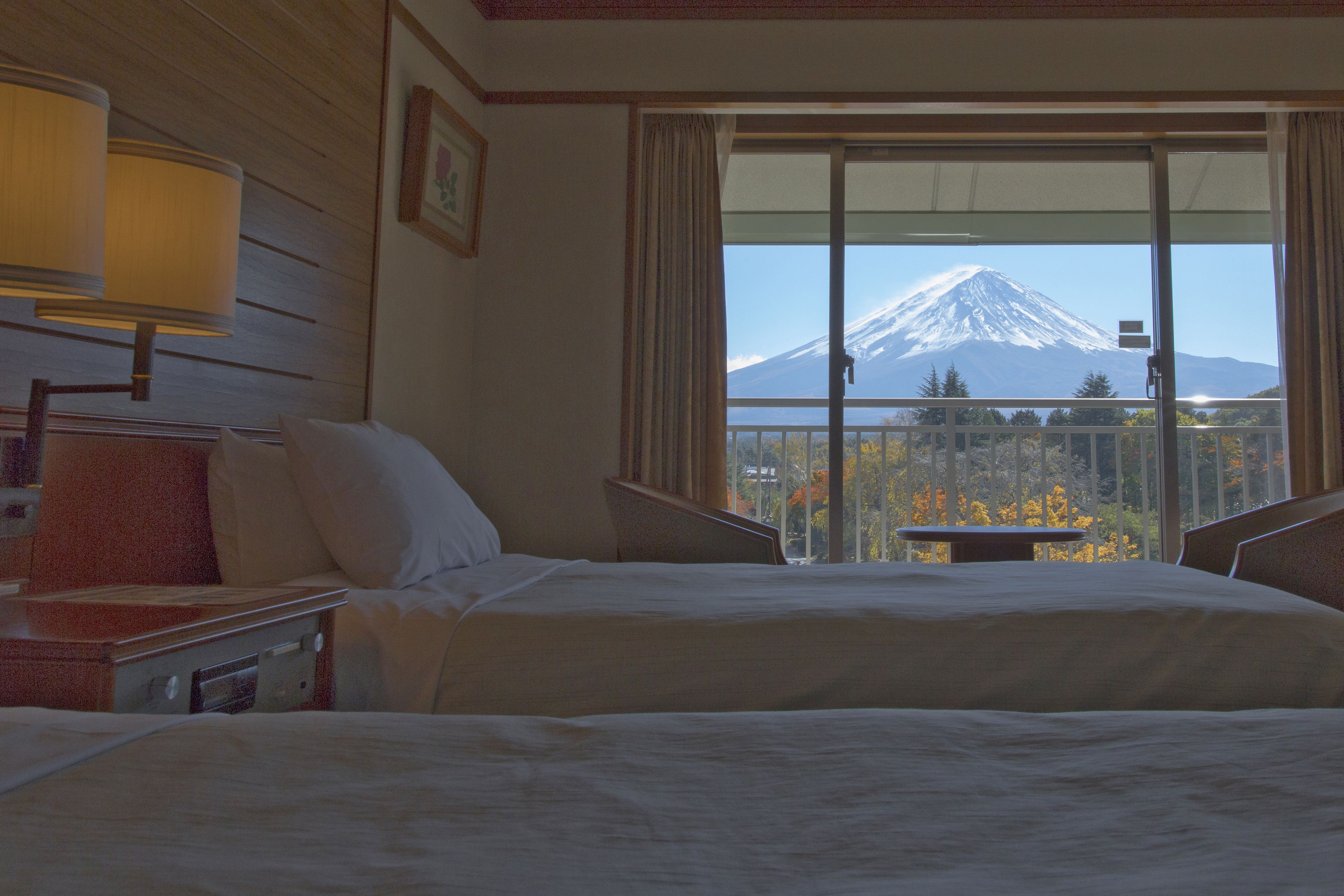 A hotel room with a bed, a nightstand, a lamp, and a large window offering a view of a mountain.