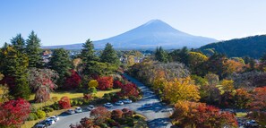 A parking lot with cars, surrounded by autumn-colored trees and a view of a mountain. - Fuji View Hotel (Fujikawaguchiko)