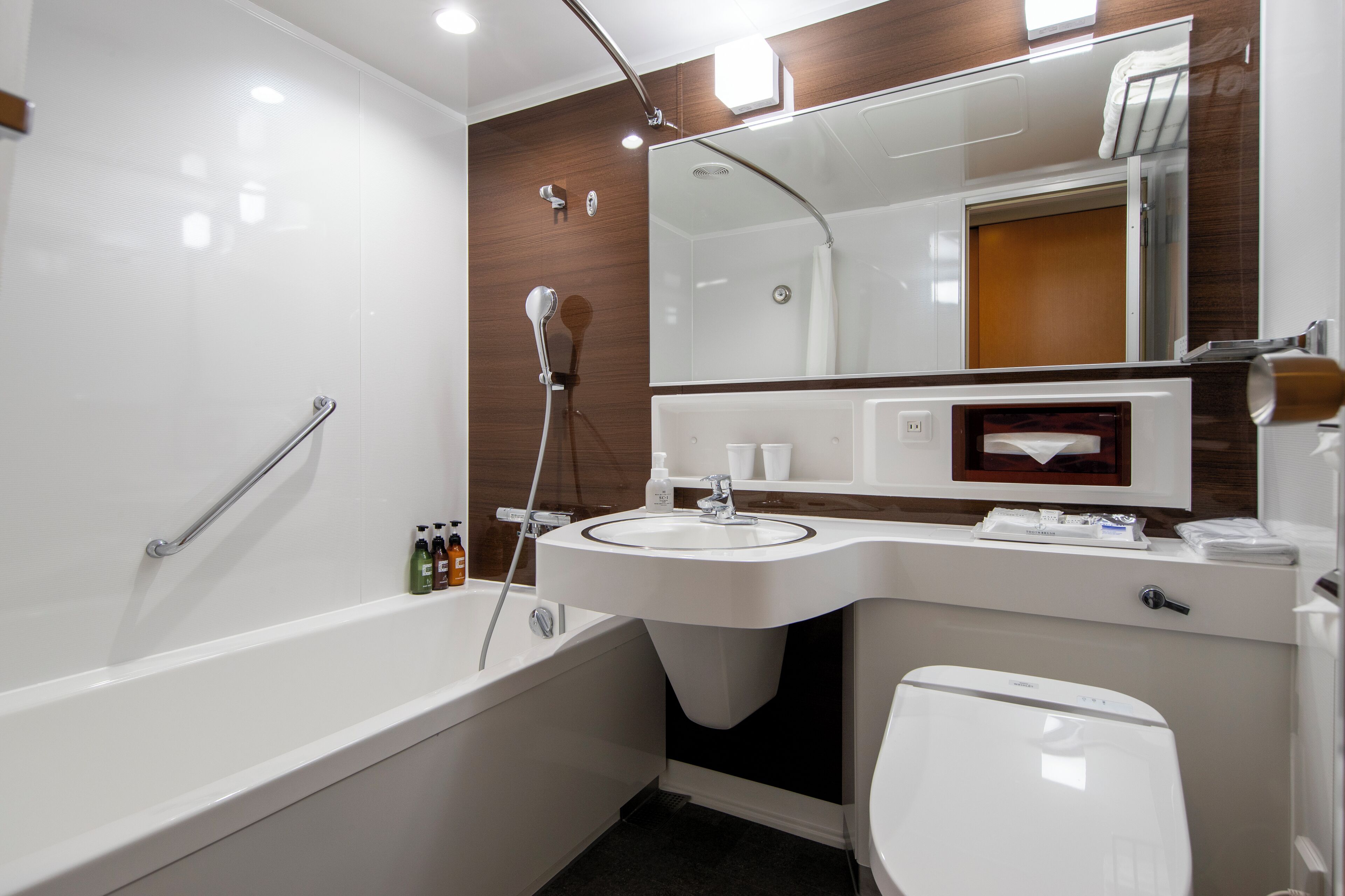 A modern bathroom with a bathtub, a sink, a toilet, and a large mirror.