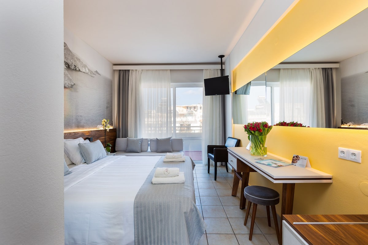Hotellihuone, jossa on sänky, työpöytä, tuoli, televisio ja ikkuna, jossa on verhot.