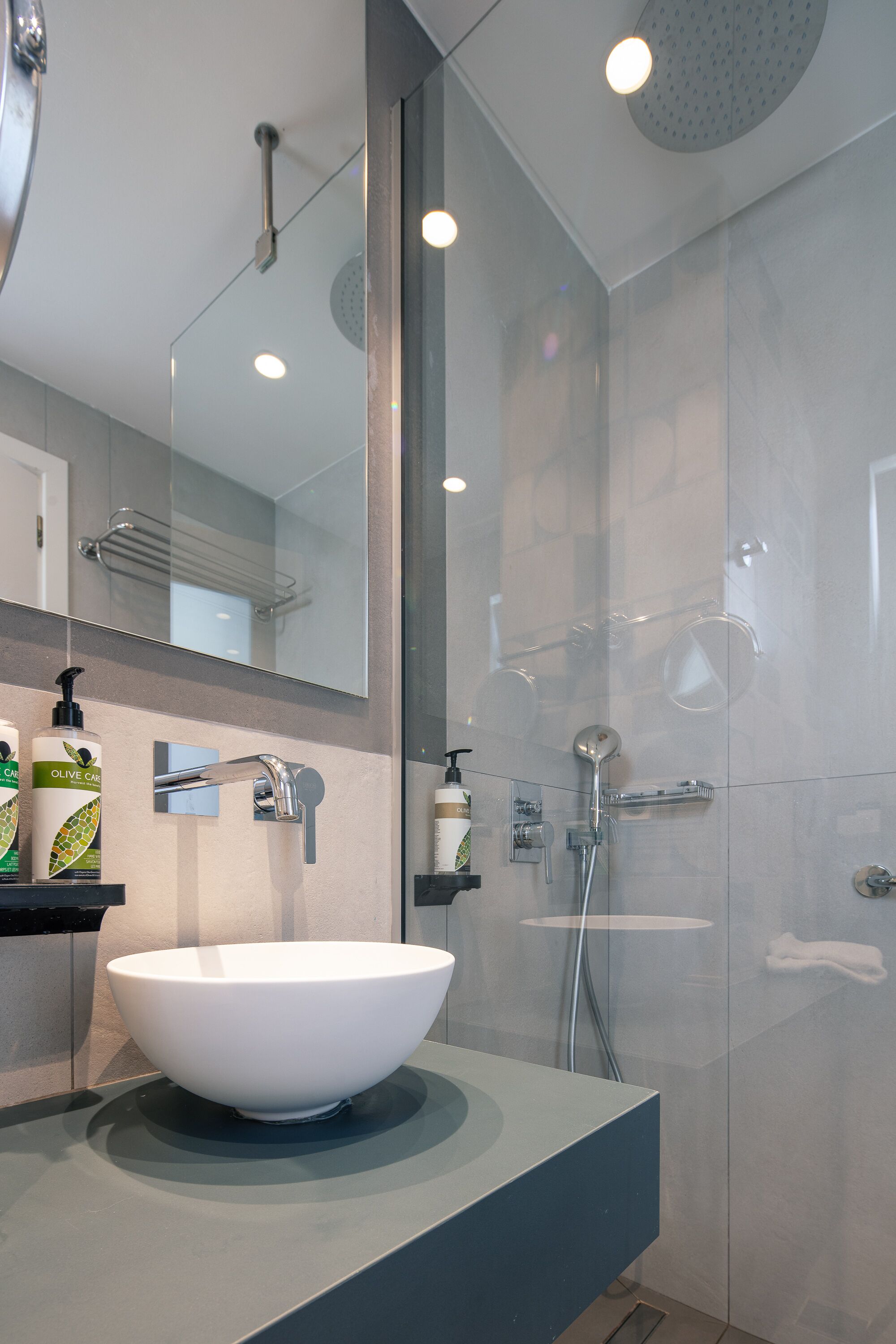A modern bathroom with a large white vessel sink, a glass-enclosed shower, and a mirror above the sink.