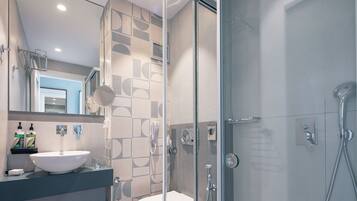 Une salle de bain moderne avec une douche à parois de verre, un lavabo blanc et un miroir au-dessus du lavabo.