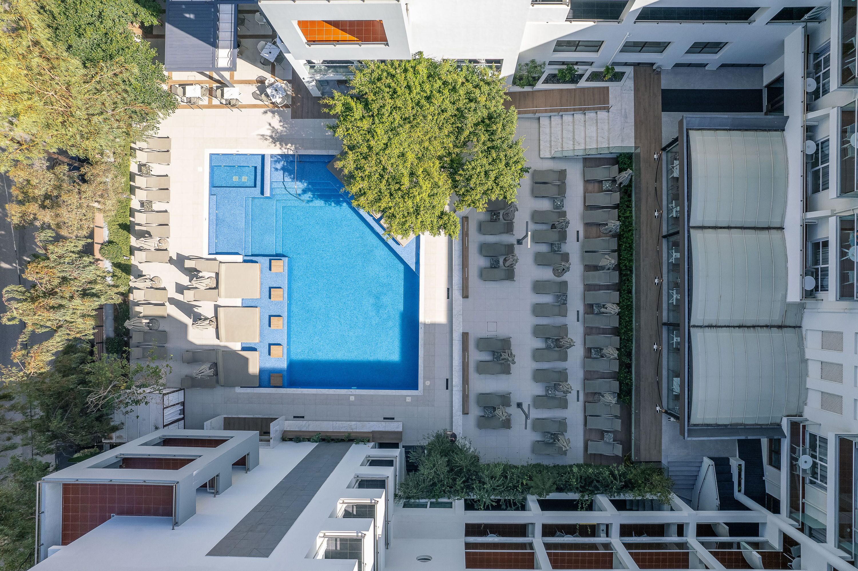 Ein Luftbild eines Hotels mit großem Swimmingpool, Außenbereichen zum Sitzen und einem Baum in der Mitte.