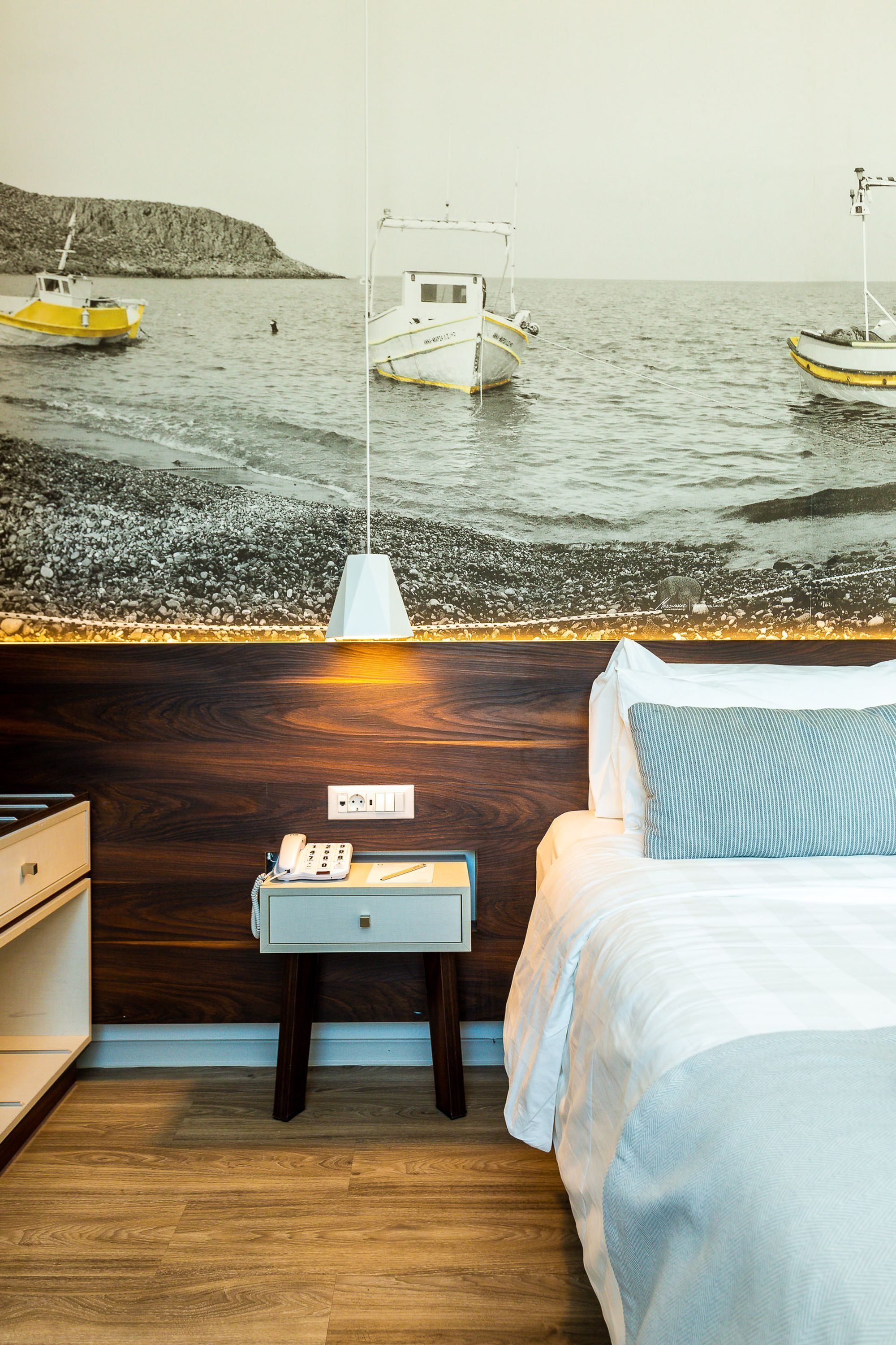 A bedroom with a bed, bedside table, and a wall mural of boats on water.